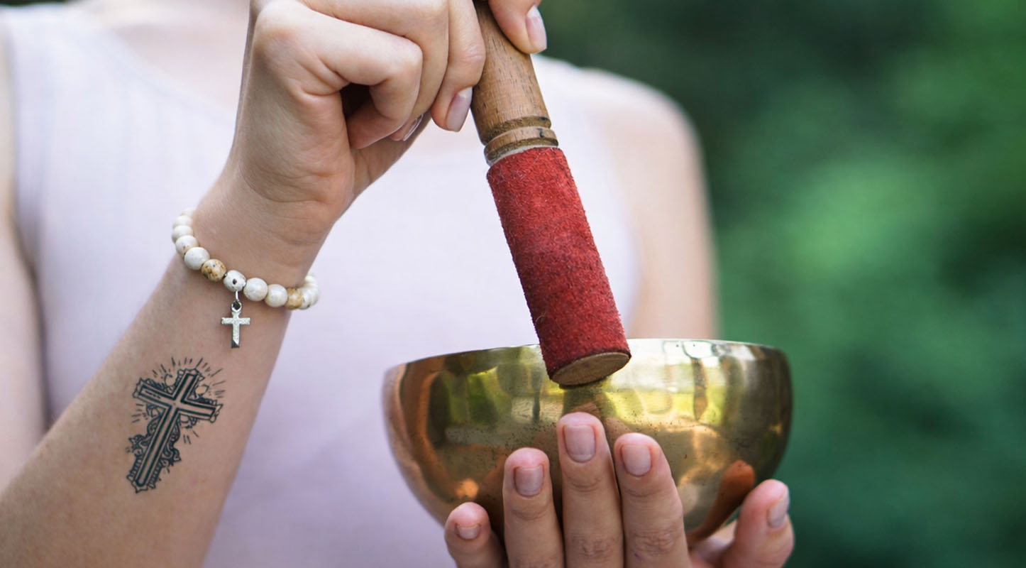 Christian woman playing a Tibetan singing bowl with cross tattoo and Christian bracelet for meditation, mindfulness and calm