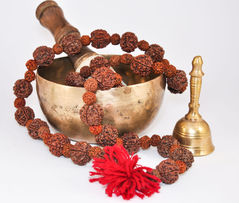 Tibetan singing bowl beside a rudraksha mala and a ritual bell, showing the difference between an instrument and consecrated ritual objects