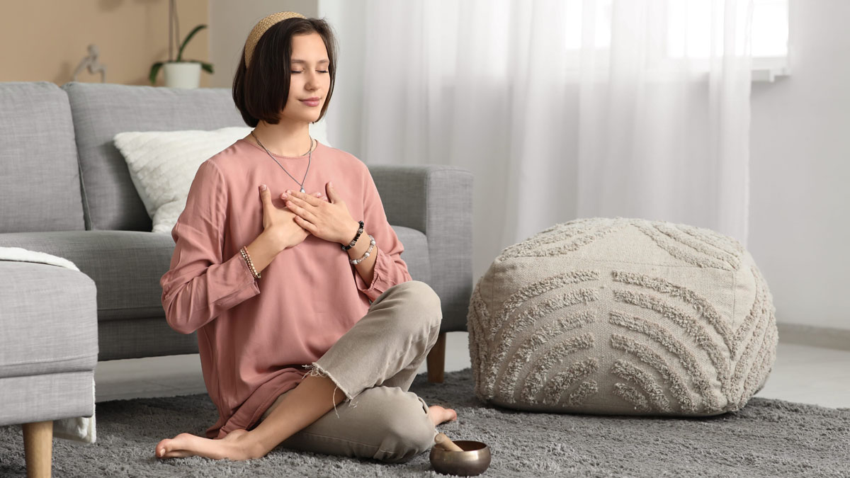 Voo breathing practice with a Tibetan singing bowl at home Woman seated on the floor with hands on her chest practising Voo breathing beside a Tibetan singing bowl