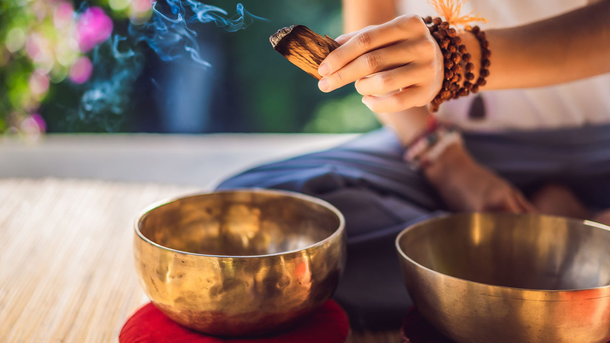 Incense burning alongside Tibetan singing bowls before a sound session Incense smoke rising above two Tibetan singing bowls resting on red cushions during a sound healing practice